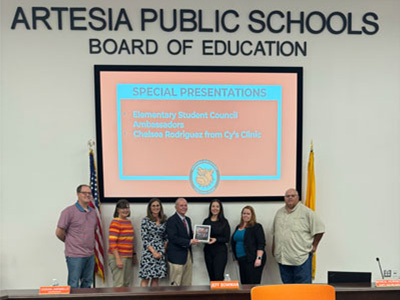 Artesia Public Schools Board of Education. Adults below a screen that reads: Special Presentations Elementary Student Council Ambassadors Chelsea Rodriguez from Cy's Clinic